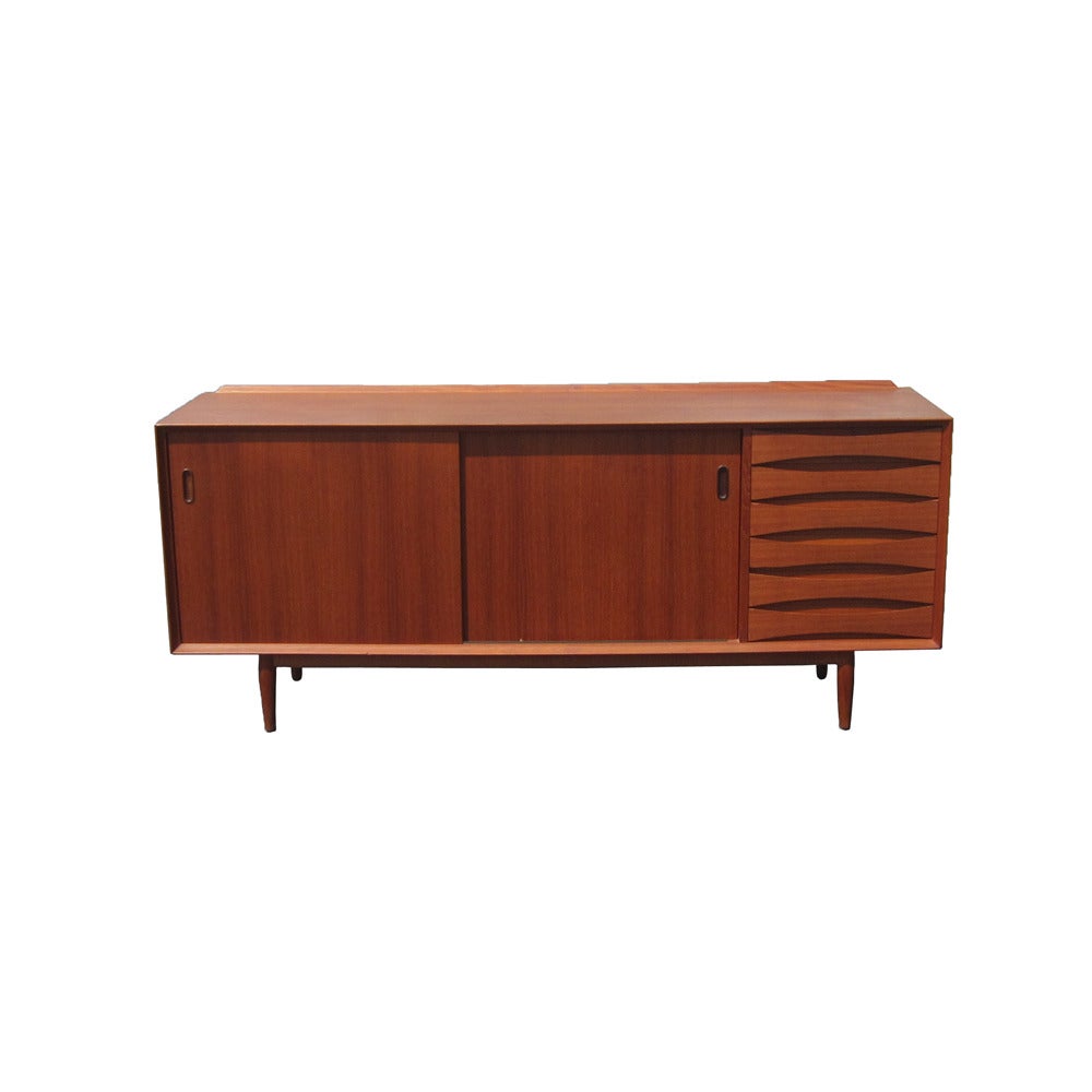 A vintage six foot Danish teak credenza designed by Arne Vodder for Sibast Furniture. Two sliding doors reversible doors open to reveal central storage area with shelves with six small sculptural drawers for smaller items on the right.