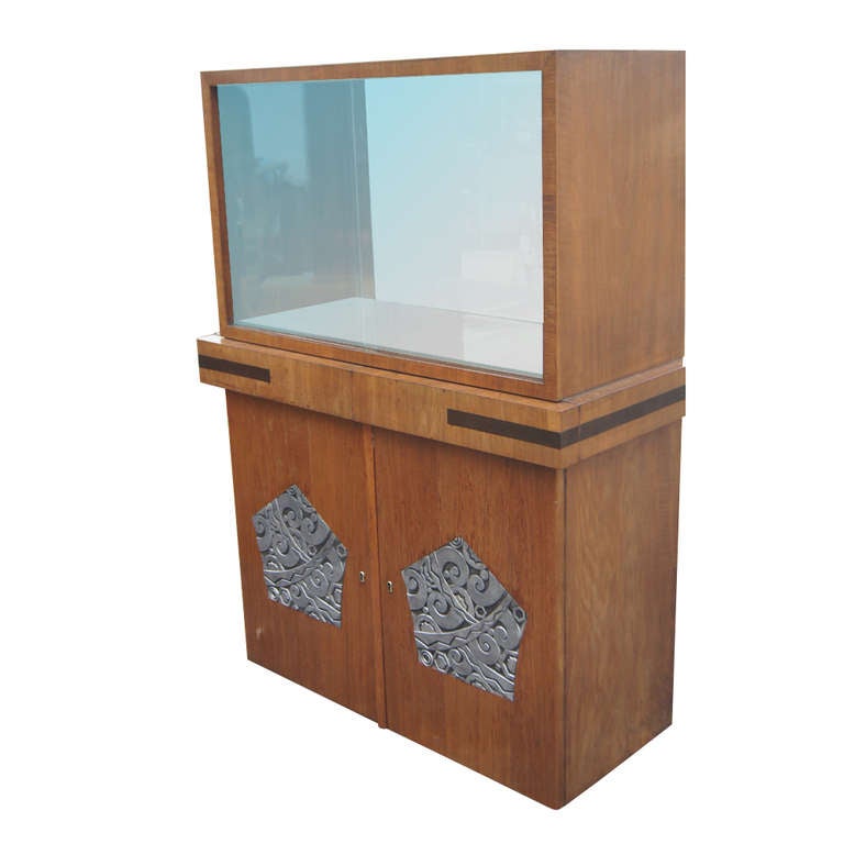 An Art Deco, two-section cabinet for china or bar storage.  The upper cabinet has sliding glass doors and a mirrored interior. The lower cabinet features two drawers and ample shelved storage. The cabinet doors feature ornamental metal appliques.