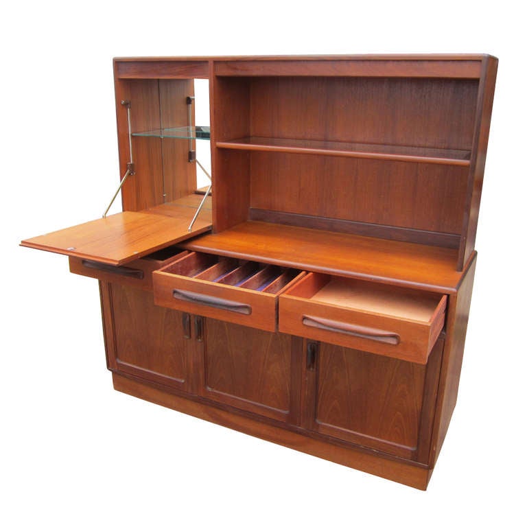 A Danish style multi-use cabinet which functions as a buffet, china cabinet and bar. The bottom section has three doors concealing shelved storage and three drawers, one of which is partitioned for flatware. The top section features shelves and a