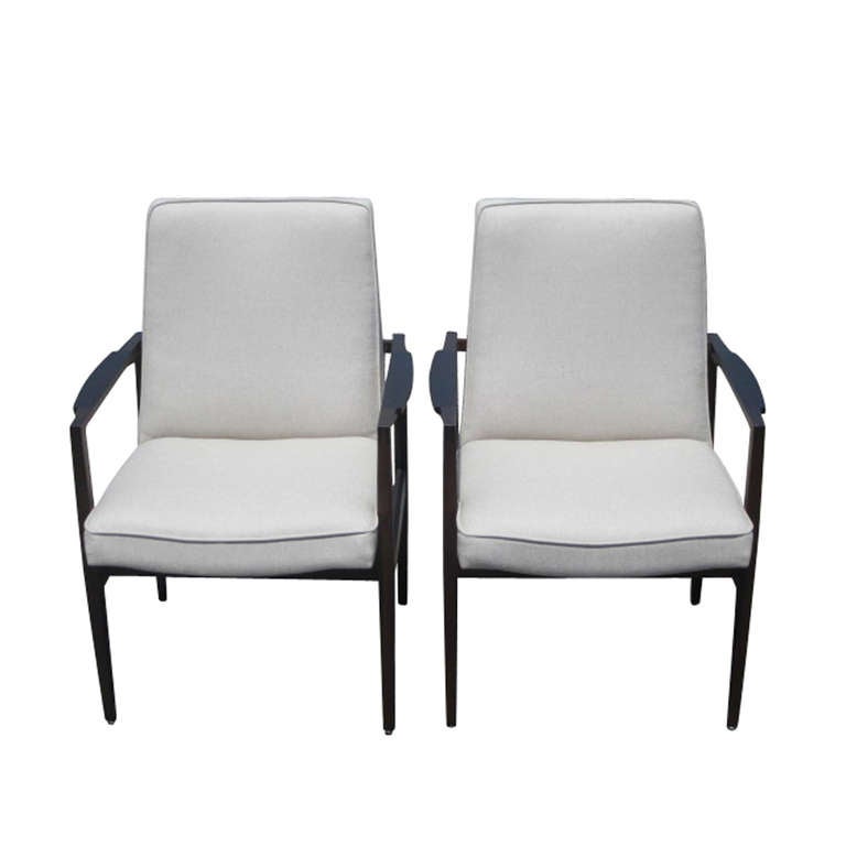 A pair of mid century Jens Risom style arm chairs.  The frames are of two-toned walnut.  Upholstered in a neutral linen fabric.