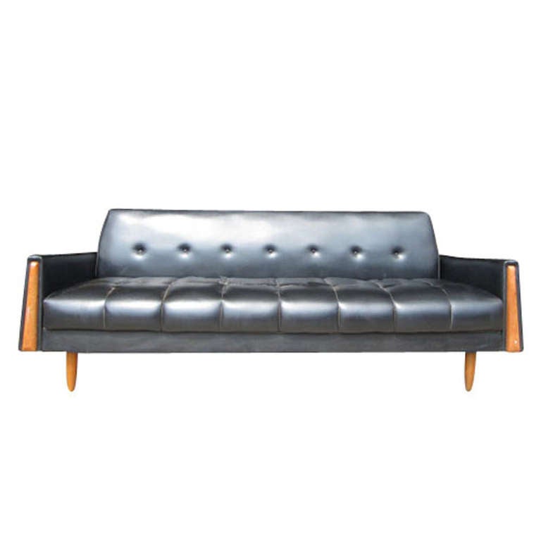 Back of sofa folds down to make a daybed 

Wooden armrest inserts 

Slim tapered wooden legs 

Black Naugahyde upholstery

Circa 1960's

Price is for (2) sofa daybeds