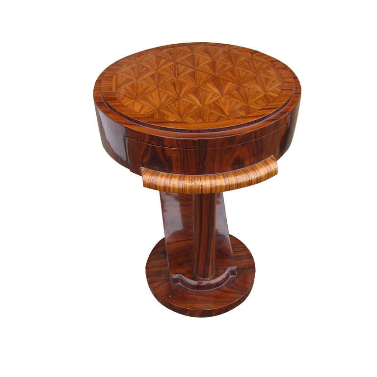 Table features round top with inlaid marquetry forming a 
geometric design supported by a single vertical column 
with a rear curvilinear support on a circular base.

Single drawer with wooden drawer pull