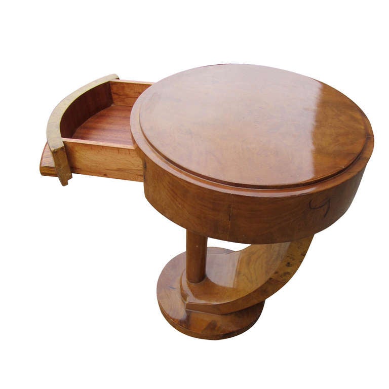 Table features round top with bookmatched burl veneer 
supported by a single vertical column 
with a rear curvilinear support on a circular base.

Single drawer with a wooden pull.