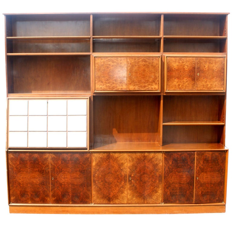 A mid century modern wall unit executed in an exotic burled veneer.  A multi-use piece containing a desk, fitted flatware drawers, and extensive shelved storage both open and concealed. The burl is quite stunning.

White leather insets on pull out