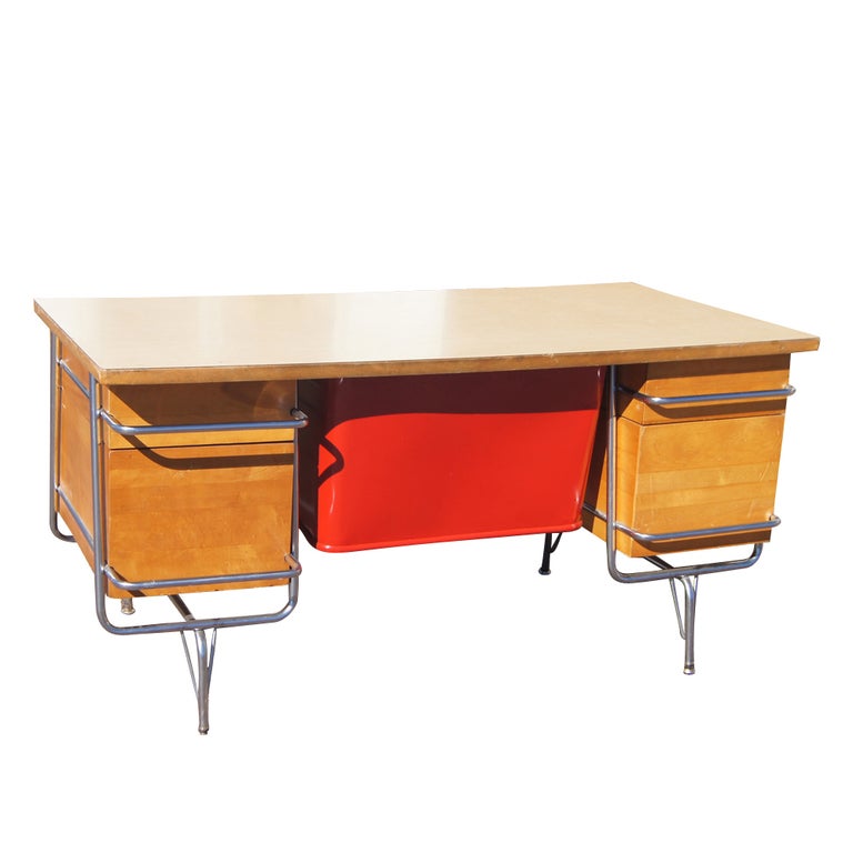 A mid century modern desk designed by KEM Weber and made by Heywood Wakefield.  A chrome tubular frame with birch drawers, laminate top, and red metal modesty panel.