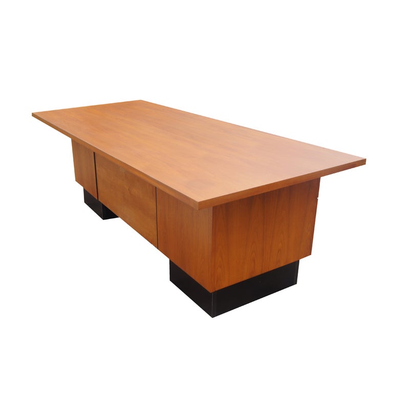 A mid century modern desk designed by George Nelson and made by Herman Miller. Walnut construction with four drawers on double pedestal black plinth supports. 

83