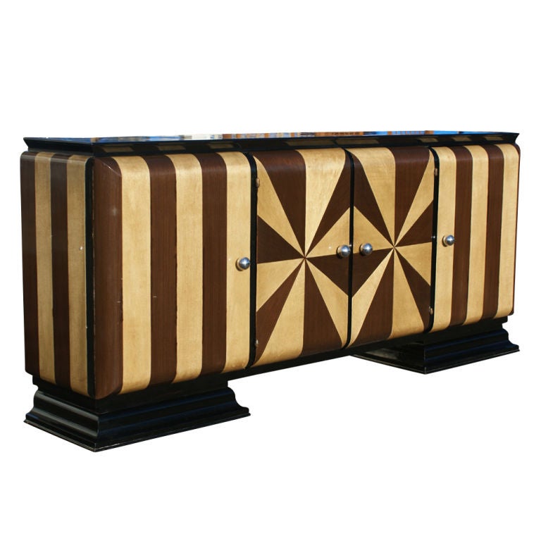 An Art Deco buffet inlaid with contrasting wood veneers in an exuberant pattern with an ebonized base.  Two center doors concealing four drawers with burled wood fronts.  Two side doors with shelved storage.