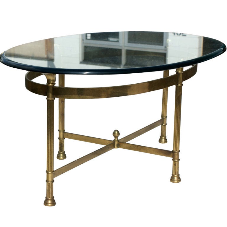 A neoclassical style cocktail or side table with a brass base and oval 3/4" glass top.  Reeded legs with acanthus leaf brackets supporting the top.