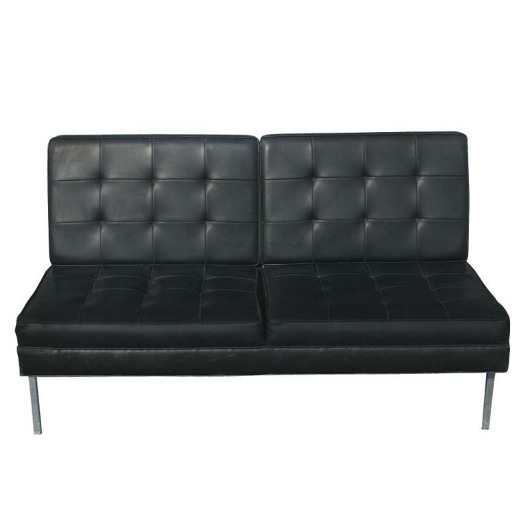 A mid century modern armless settee in the style of Florence Knoll.  Chrome base with angled rear legs and tufted black vinyl upholstery.