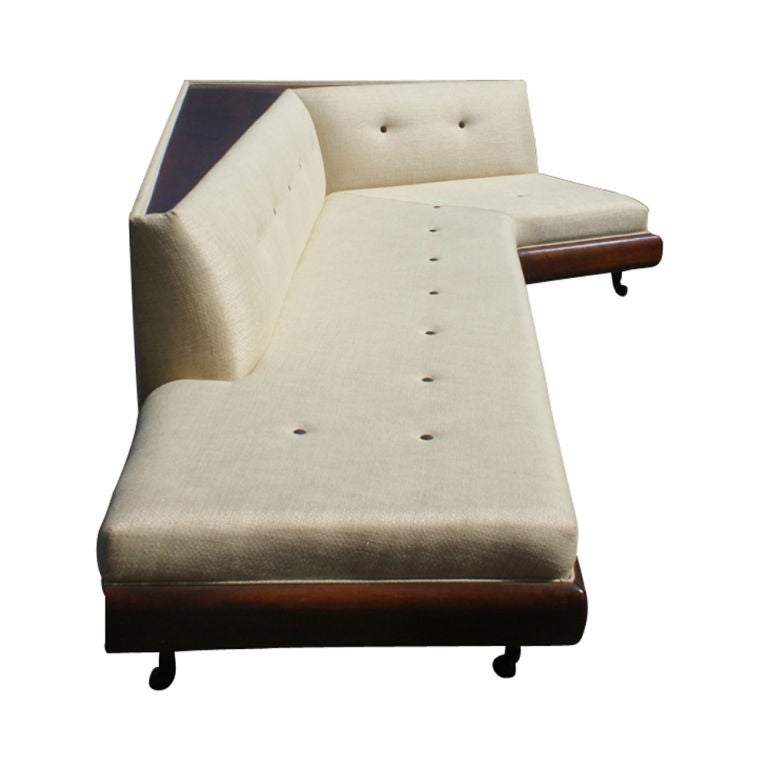 A mid century modern corner sofa designed by Adrian Pearsall and made by Craft Associates.  A walnut base with buit-in walnut back shelf.  Newly upholstered in tufted beige fabric with brown accent buttons. Two are available, 2nd sofa requires