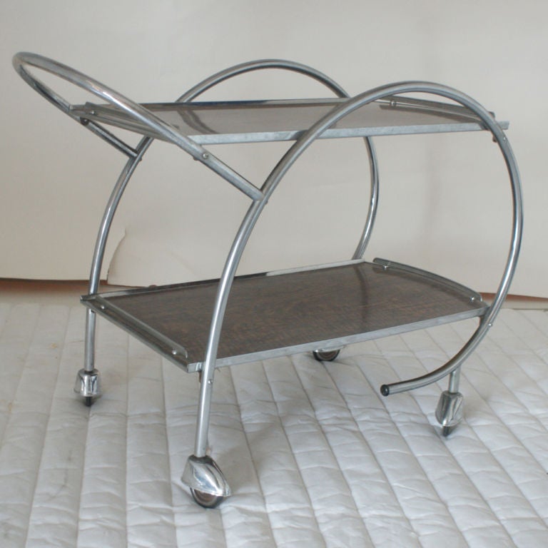 An Art Deco tea trolley or bar cart with a curved tubular chrome frame and two faux wood shelves.