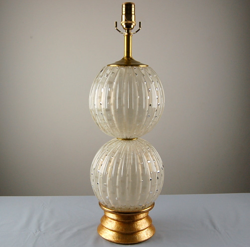 Elegant Murano glass lamps imported by Swank Lighting, handblown by the best Italian artisans. A duo of stacked balls in VANILLA filled with GOLD dust and controlled bubbles, mounted on gold leaf wood bases. 

They stand 24 inches from tabletop to