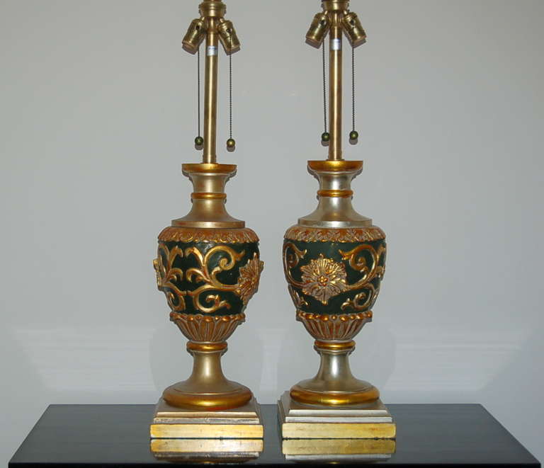 Hollywood Regency at its best, courtesy of The Marbro Lamp Company.  Carved wood adorned with SILVER AND GOLD LEAFING, against a DARK GREEN background.  The carvings are identical, coloration slightly variable. 

The lamps stand 35 inches from