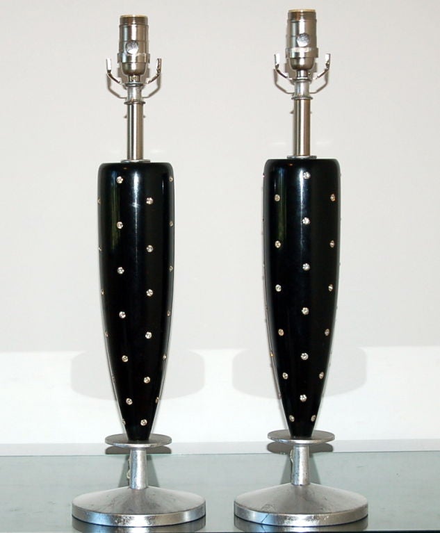 The padded shoulder, narrow waisted Silhouette give these lamps a classic look. The columns are black lacquer studded with rhinestones, the bases are silver leafed. 

The lamps measure 26 inches from tabletop to socket top. As shown, the top of