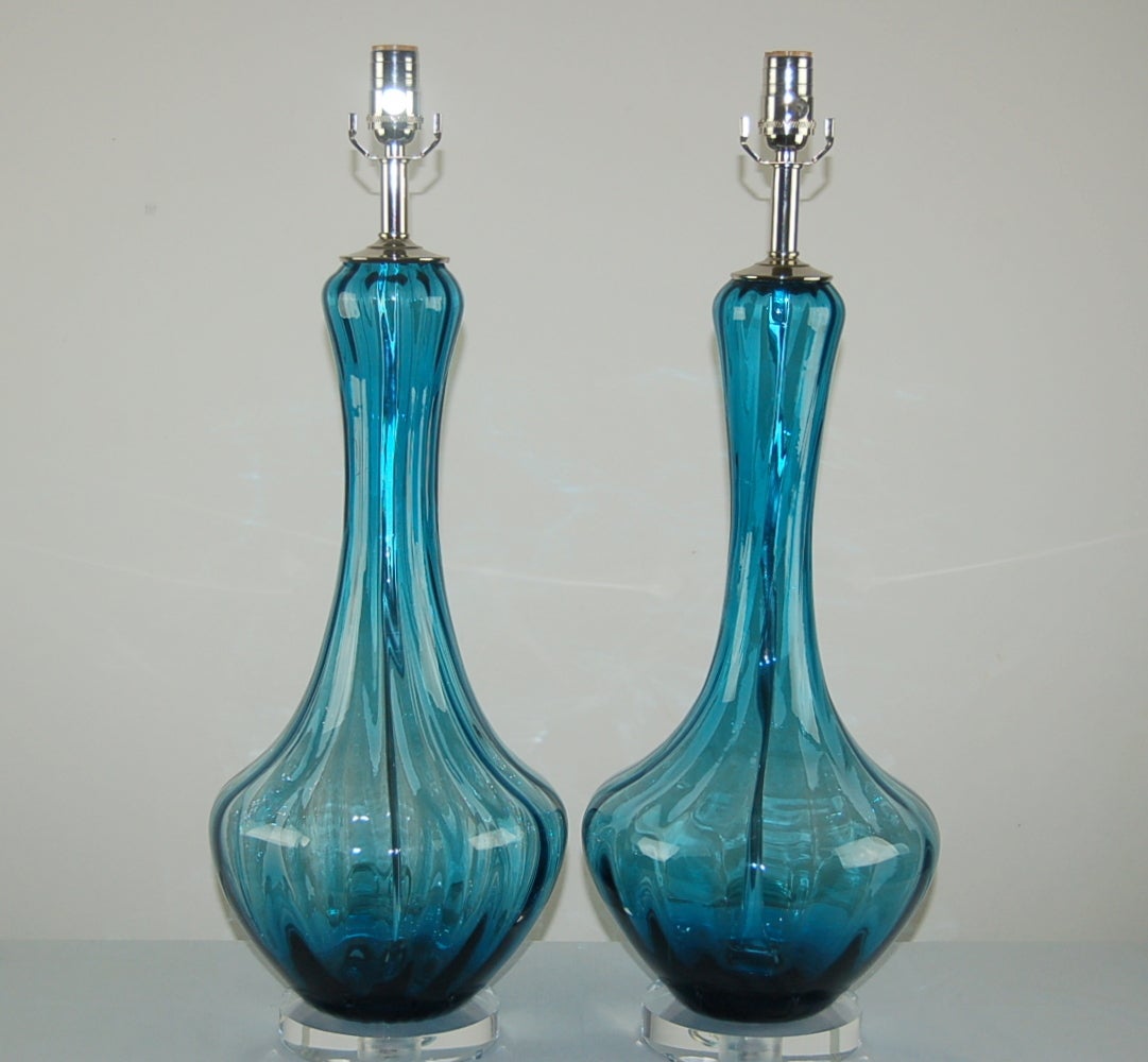 A spectacular pair of TEAL BLUE Murano lamps with vertical optics. The rich color of the glass makes these lamps so special! We show them on a thick round of Lucite. 

The lamps stand 27 inches from tabletop to socket top. As shown, the top of