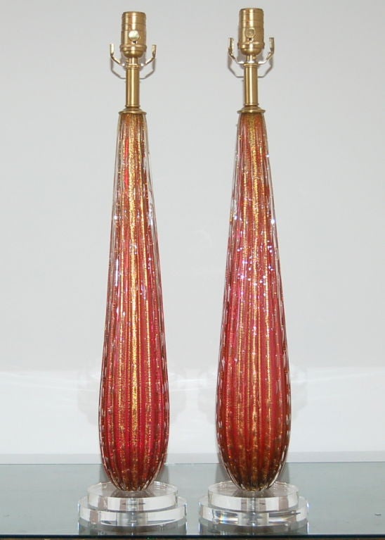 These beautiful cranberry Murano lamps are filled with gold dust and controlled bubbles. Vertical ribs add wonderful texture and depth to the simple teardrop shaped columns. The lamps are 27 inches from tabletop to socket top. As shown, the top of