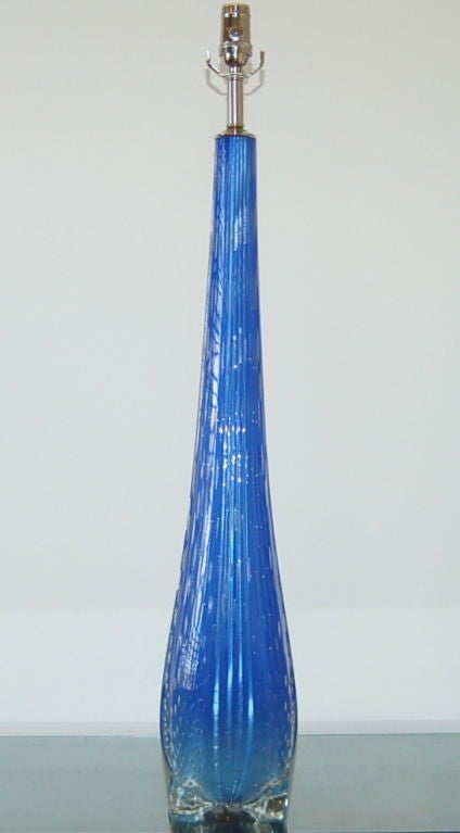 This beautiful royal blue Murano lamp has vertical ribs and controlled bubbles throughout. It sits on four paddle-like feet and has the style and whimsy of a John Dickinson table.

The lamp stands nearly 36 inches to the socket top. As shown, the