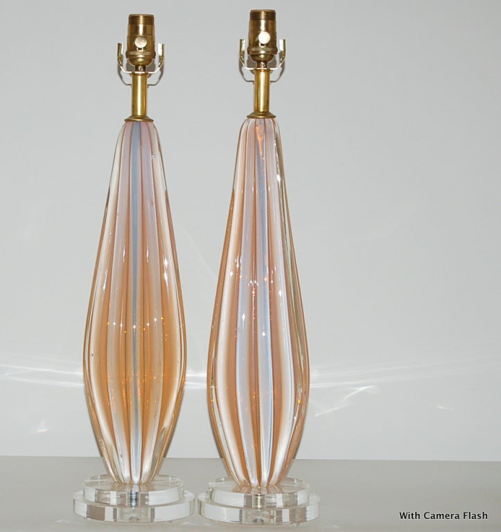 Thickly ribbed pair of vintage Murano lamps in Peachy Cantaloupe. The color of the glass changes as the ambient light shifts, courtesy of the opaline, check out our photos for color variations. 

The lamps stand 24 inches from tabletop to socket