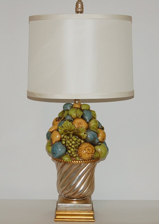 A spectacular arrangement of hand-painted fruit fashioned from Italian ceramic by The Marbro Lamp Company, circa 1963. Rich colors of Ocher, apple green, and teal blue in a champagne and silver urn. 

The lamp stands 36 inches from tabletop to