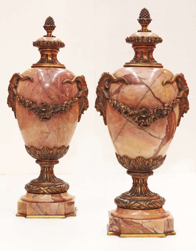 a pair of bronze mounted pink marble urns with swags and ram's heads which rest on quatrefoil bases / 5.5
