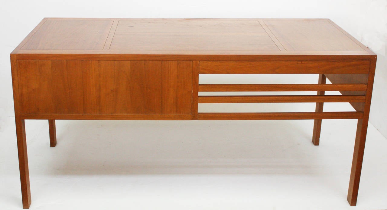 A mid-century modern walnut desk, solid straight sided top, left-side knee-hole opening, right-side containing three drawers; two stacked small drawers next to large single drawer, which has removable slanted wood dividers.  One-half of desk front