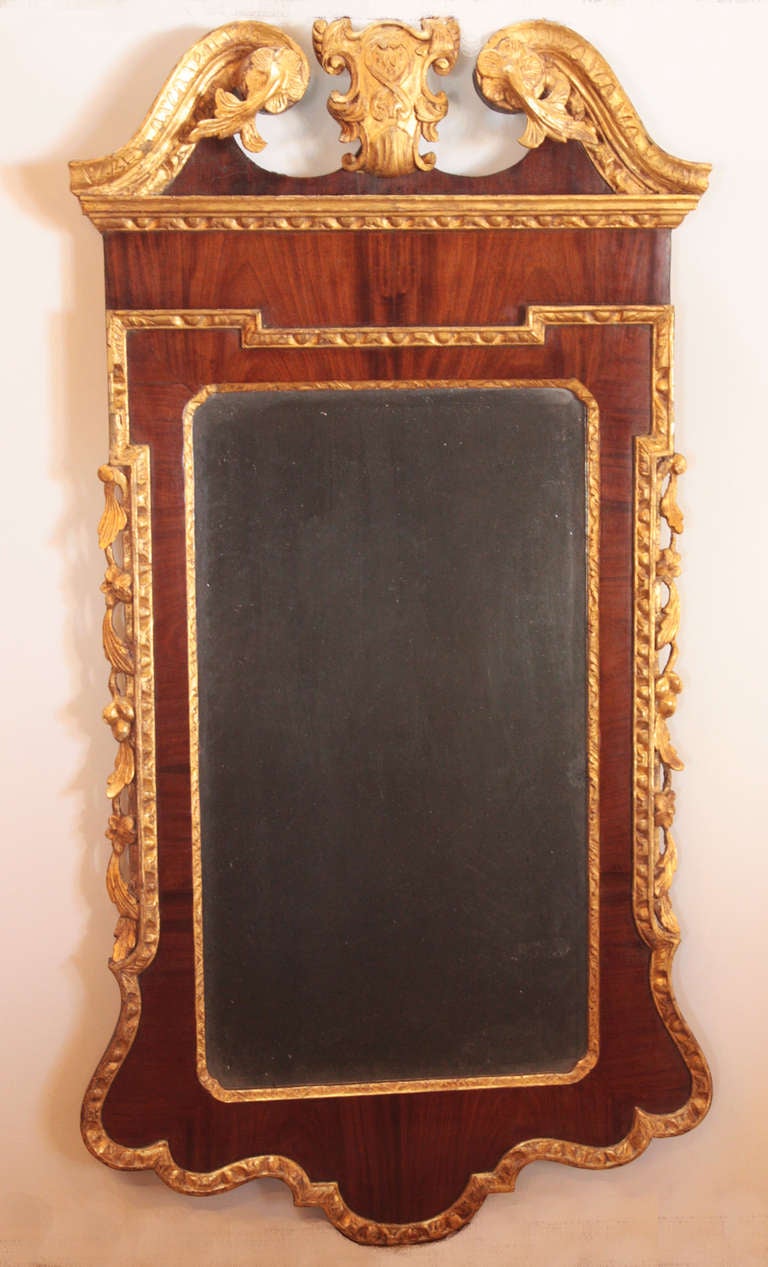 a George II mirror frame of mahogany with gilt embellishments outside, inside and top, broken pediment with centre shield in gilt