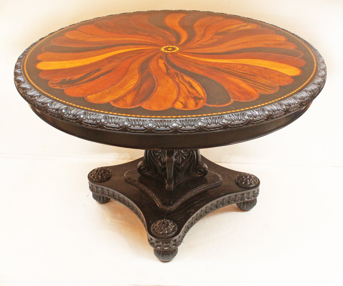 a rare Anglo-Indian /  Ceylonese ebony and specimen wood center table with circular tilt–top inlaid with a center star medallion issuing a radiating spiral of specimen woods, including rosewood, coromandel and palm, each divided by a banded veneer,