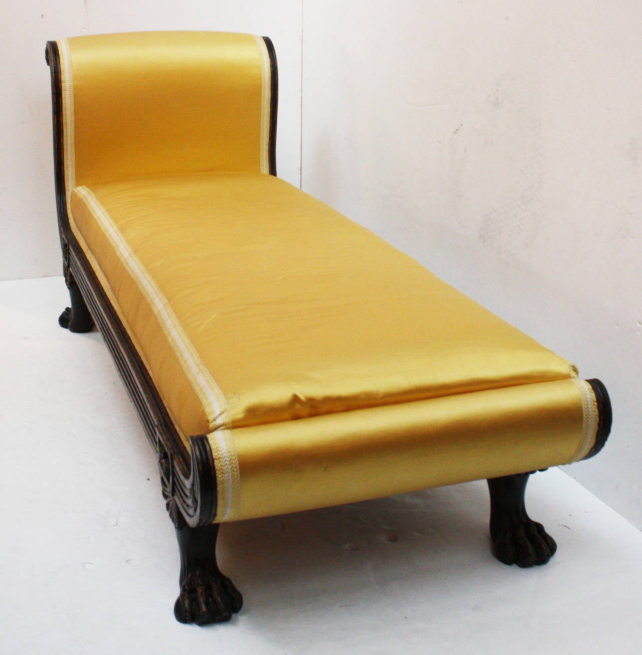 an English Regency Recamier in the manner of Thomas Hope, Regency decorator and patron, black and gilt painted frame with  lion's paw feet, upholstered in pale yellow silk with loose cushion and bolster