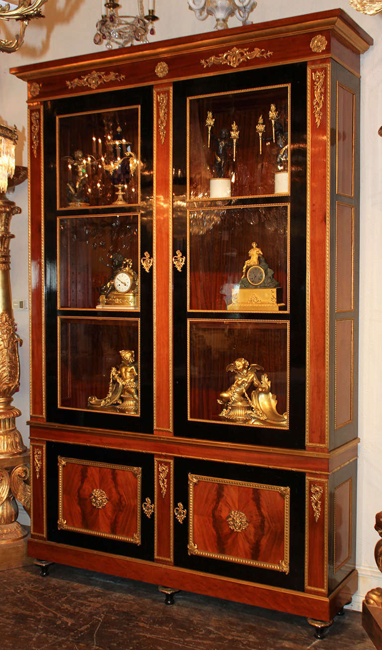 exquisite French Directoire style bookcase featuring impeccable gilt bronze detailing, narrow sized cabinet composed of authentic French polished and black lacquered mahogany, finely cast bronze mounts adorn the panels and lower cabinets, original
