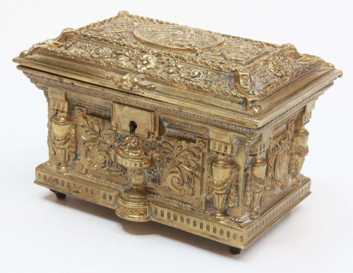 An elaborately repoussed brass box with urns and cherubs amongst foliage.  Burgundy velvet lined interior.