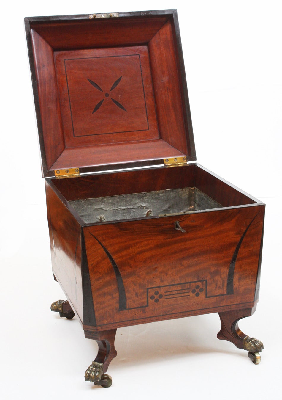 an English Regency cellarette, mahogany with black band on lid, raised center of lid has flame mahogany with stenciled line and dot matrix, as does body, the whole stands on feet with brass paw shoes and castors, with fitted interior