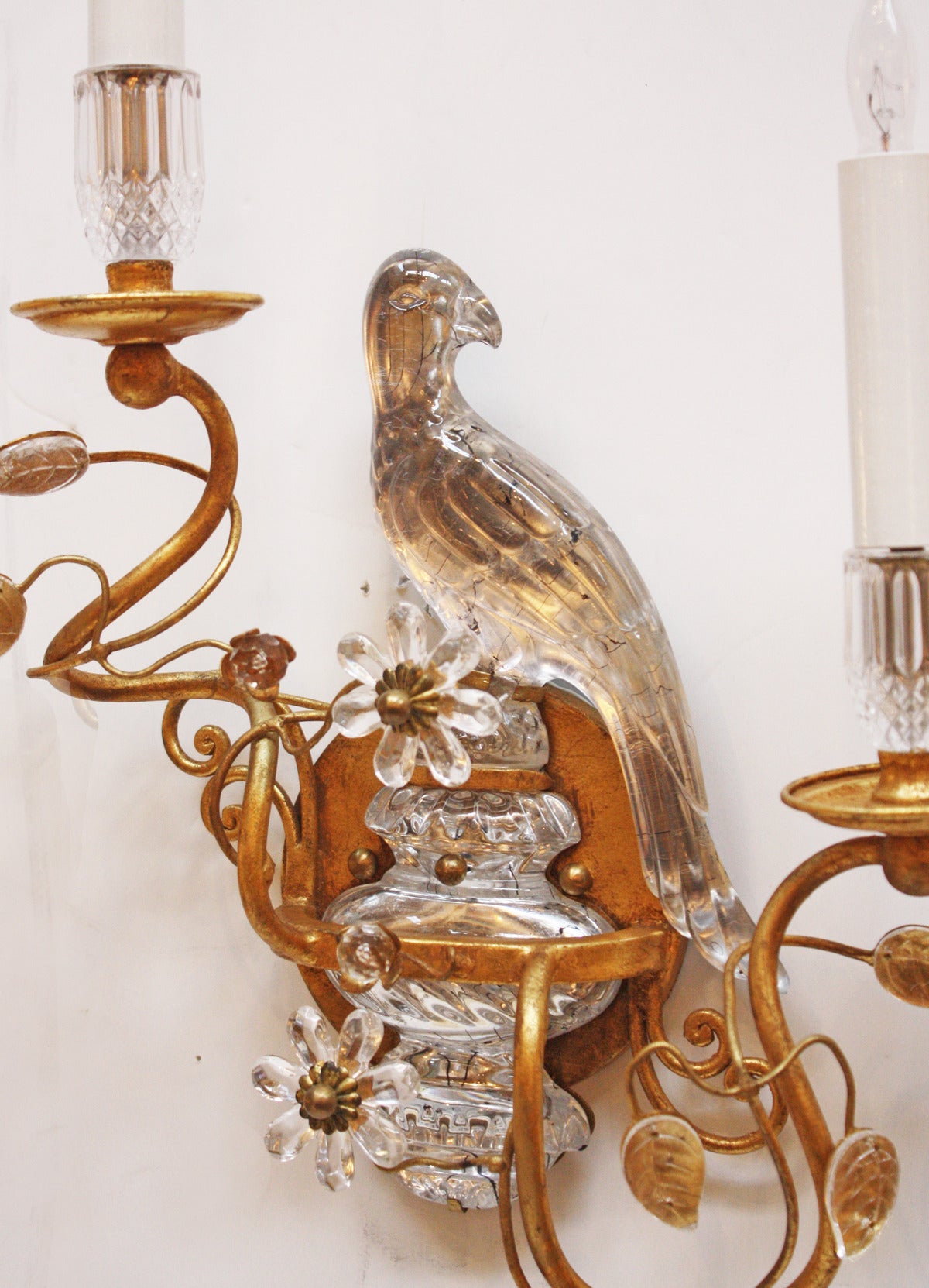 A pair of gilt metal two-light Maison Baques stlye sconces, crystal leaves on arms and bird atop urn at back.  France  20th Century