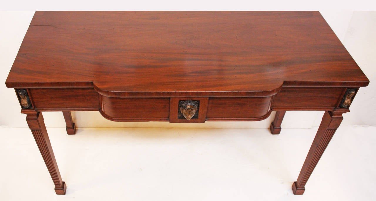 an English Regency serving table in the Egyptian taste, mahogany with crotch mahogany top, drawer added in center of apron, carved gilded and ebonized busts on sides and large head in center, reeded legs with block feet, evidence of a gallery on back