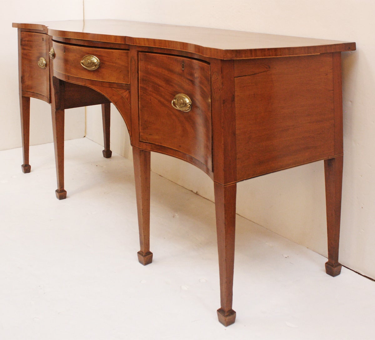 an English Georgian serpentine front mahogany sideboard with inlay banding at top corners, around each drawer, with conch shell inlay detail between drawers, straight tapered legs with spade feet.