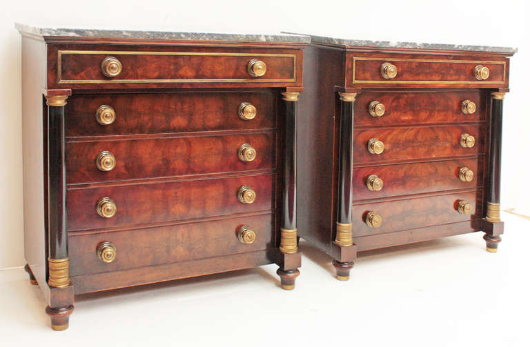 a pair of Empire style five drawer chests of mahogany, columns at sides with gilt bronze mounts, grey and  white marble tops.

French,  20th Century