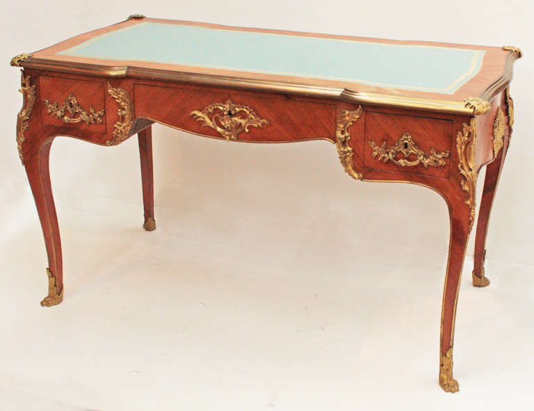 a Louis XV style writing table / bureau plat, fruitwood with ormolu trim, three drawers, green blue leather writing surface embossed and gilded