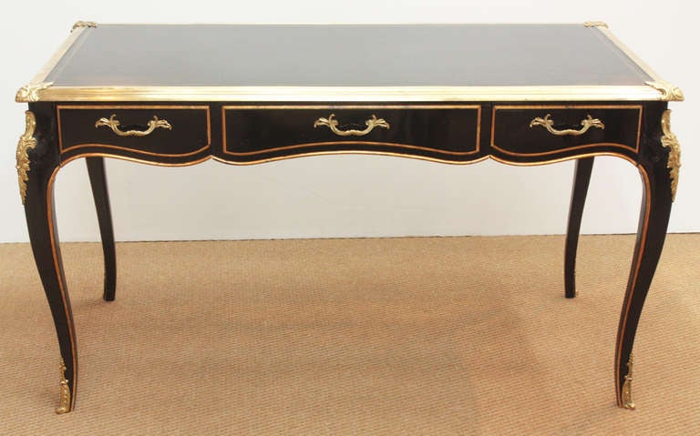 a black lacquer Louis XV style bureau plat with brass feet, mounts, hardware, and trim around the top, writing surface is black leather with gilt embossed trim 

Collector's Edition by Baker
Baker Furniture