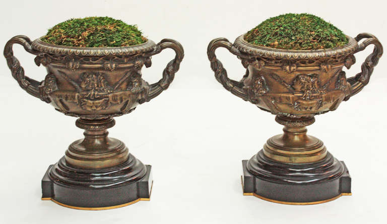 a pair of cast bronze Grand Tour urns / Warwick Cups with classical busts in high relief on body, entwined handles, the whole  mounted on black marble bases