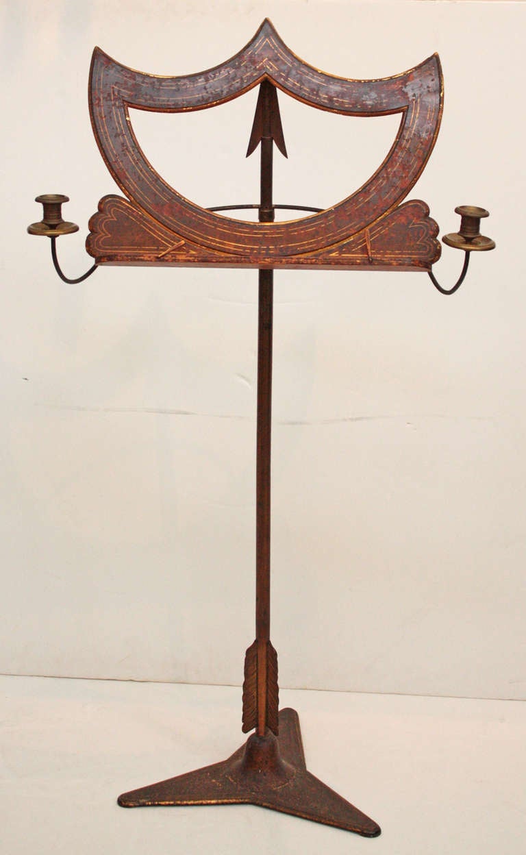 a circa 1810 / Regency period music stand with adjustable softened shield form of painted wood, brass candle holders at sides, pole support is in the form of an arrow pointing upward, metal triangular base

base is 16.5