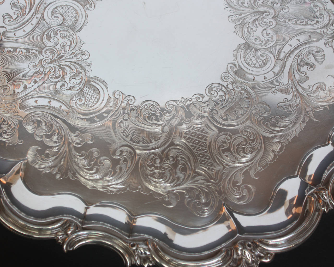 A large round sterling silver tray, Chippendale style, with elaborate scalloped border interspersed with decorative scrolls and leaves, hand engraved with blank center cartouche, resting on raised acanthus leaf and scrolled feet, mark of Jos.and