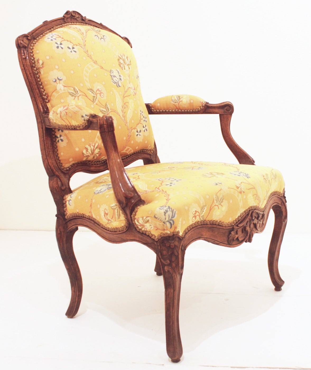 A  Louis XV period arm chair made of walnut with shaped back and seat, curved arms and apron. It is excellently carved with detailed floral and foliate motif. The chair is raised by cabriole legs ending in pad feet. The back and seat are upholstered