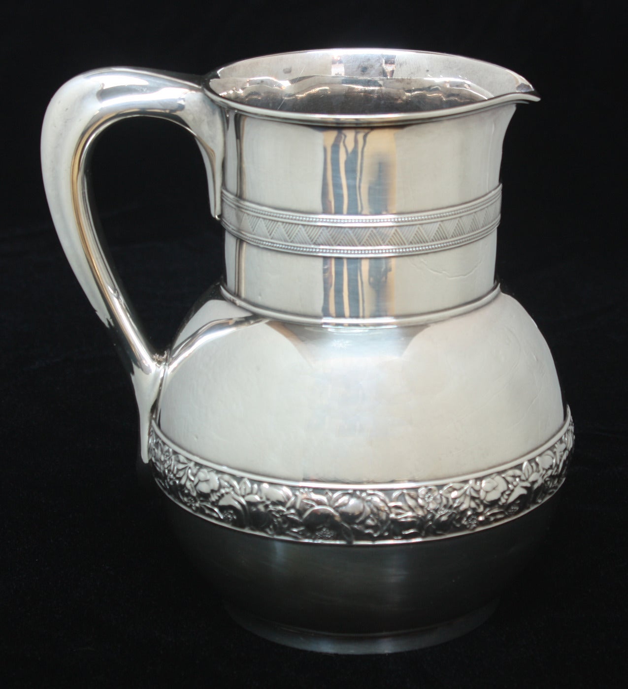 A Tiffany & Company Sterling Silver Water Pitcher / Horse Racing Trophy.  A straight neck with decorative geometric band of striated triangles, over a globular body, with  a centered decorative band of repoussed pomegranates and leaves against a