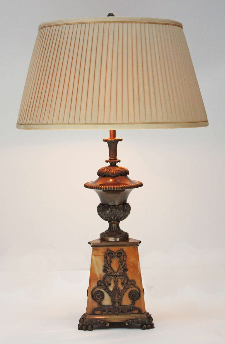 a handsome lamp with triangular gold marble base with gilt bronze decoration including feet, a bronze urn form tops the marble plinth

shade is 8.5