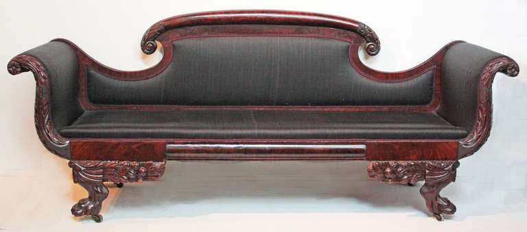 a commodious / welcoming flame mahogany sofa with black horsehair upholstery, American Classical, having a heavily carved frame, elaborately carved feet with fruit, flowers and leaves above large paws with castors