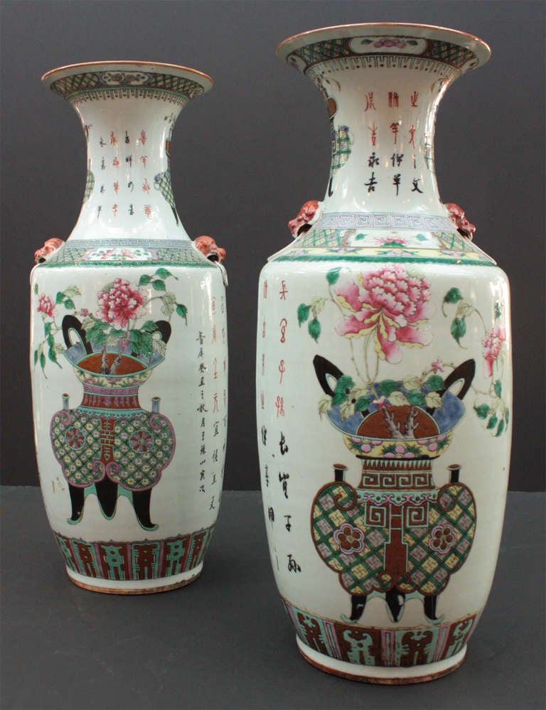 a pair of large Chinese porcelain vases, white background with multicolor jardinerres with trees on fronts and necks along with Chinese characters at sides and tops, foo dogs with rings 