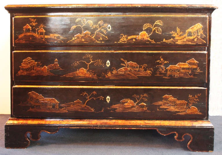 An English three drawer chest. Black background with gilt Chinoiserie decoration with flat and raised trees, rocks and houses on top, drawer fronts and sides. The whole stands on bracket feet.