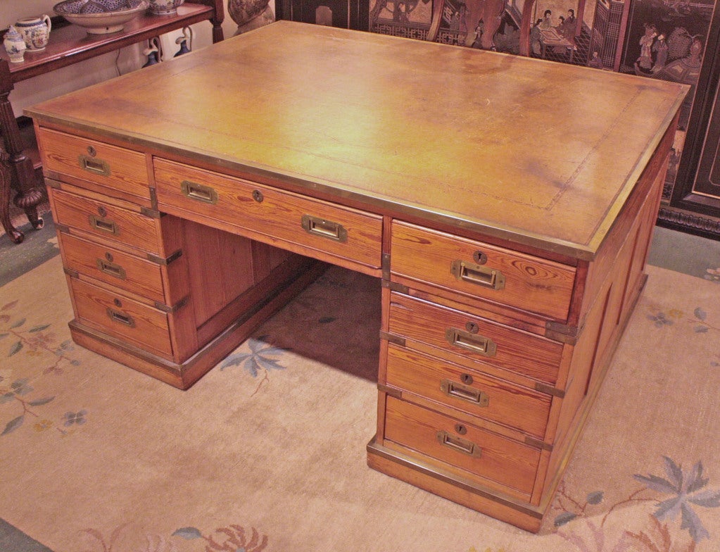 a large pine partners desk with embossed leather top with brass edge, campaign type pedestal desk / library table with four drawers on either side of opening and one center drawer on one side, the other side has cabinet doors on either side of