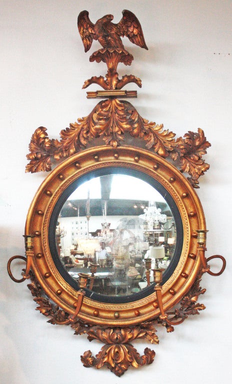 an English Regency Period giltwood convex mirror with four candle arms surmounted by swags of foliage and an eagle