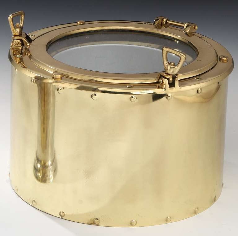 A very stylish and unusual all-brass ‘Porthole’ wine or Champagne cooler, the barrel form in highly polished brass, the ‘porthole’ with two ‘dogs’ or threaded latches with a glass central window, so you can see the contents, and a lift out liner in