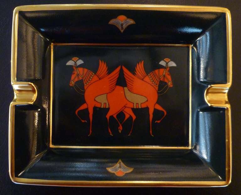 An oblong white porcelain, limited edition cigar ashtray of typical style with decoration of two red mythical winged horses, on a black background with gilt detailing. Marked HERMÈS PARIS to one side and MADE IN PARIS to the opposite with a suede